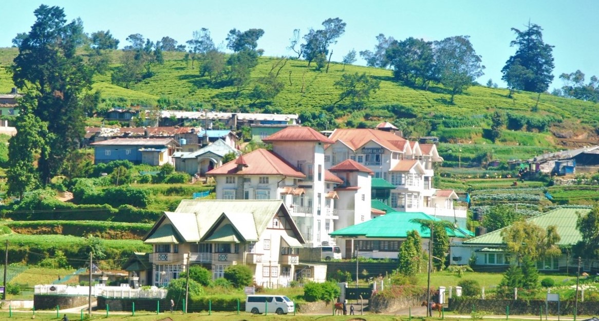 Hillside town with white and red-roofed buildings surrounded by green terraced fields under a blue sky