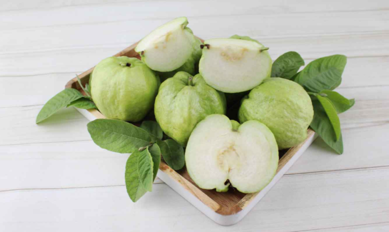 Fresh green guavas, whole and sliced, with leaves on a wooden tray, bright and fresh mood